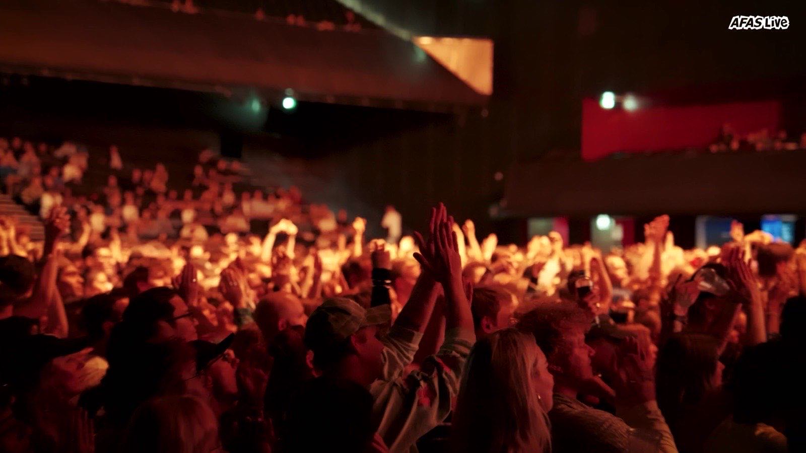 Audience clapping under red stage lighting during a concert at AFAS Live.