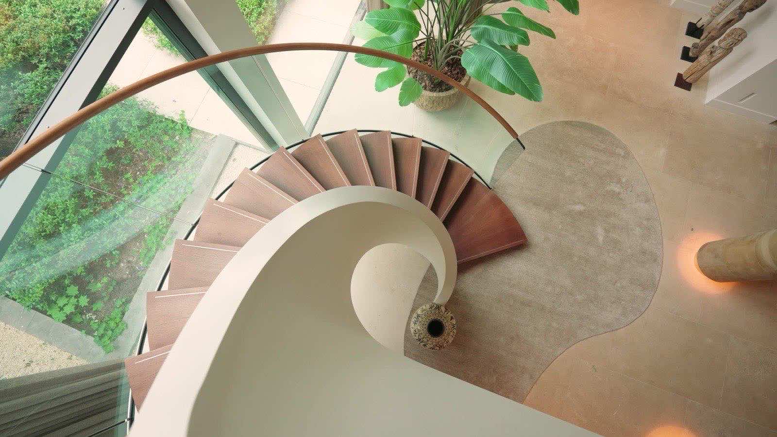 Looking down a spiral staircase with wooden treads and a white curved balustrade.