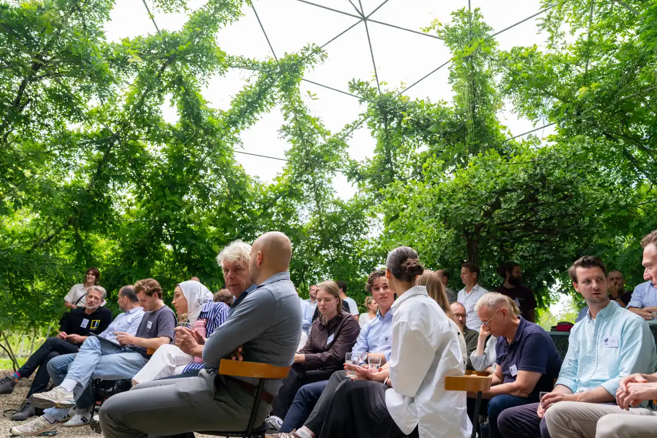 An audience seated outdoors under trees during a talk