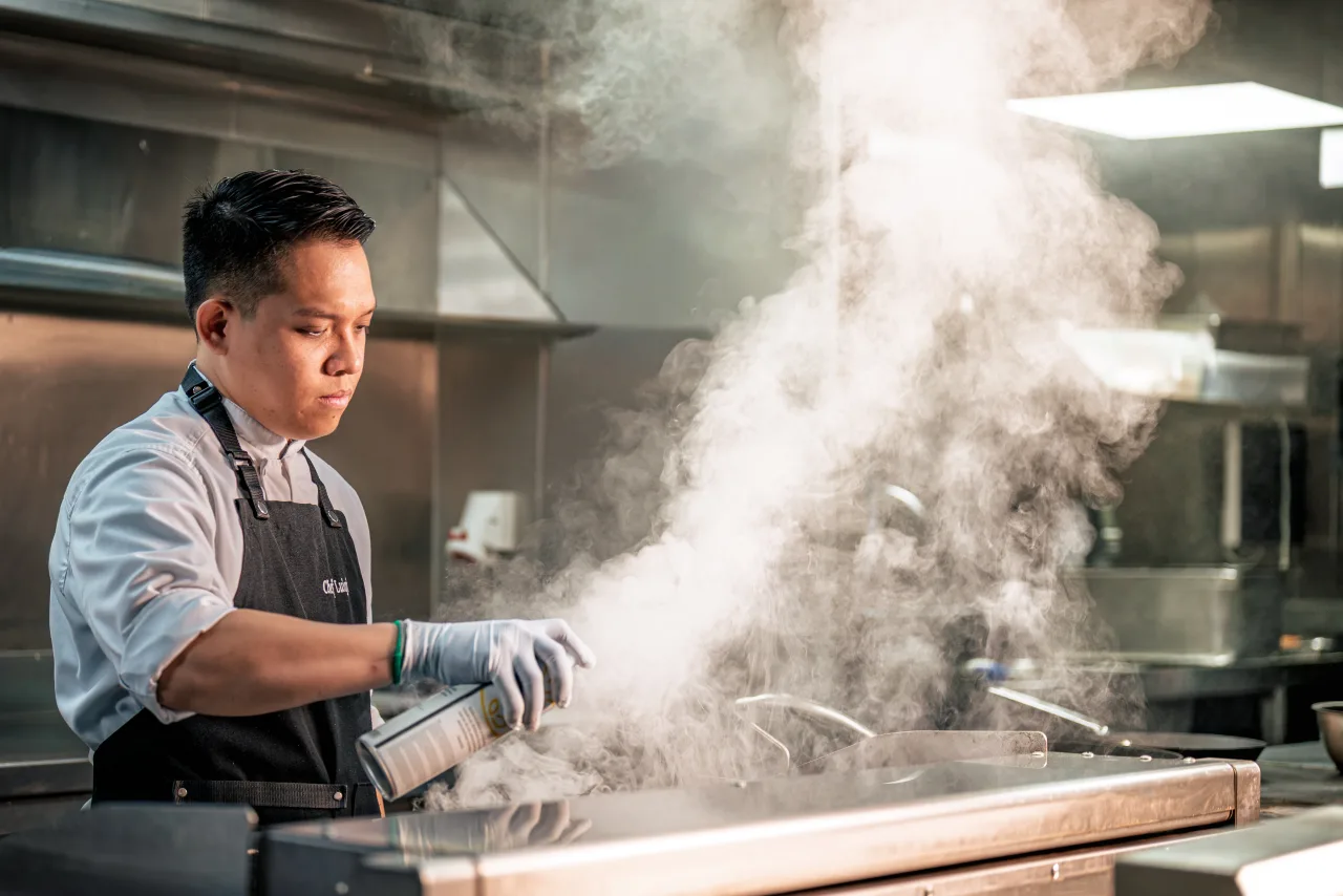 A chef working at the pass as steam rises from the counter