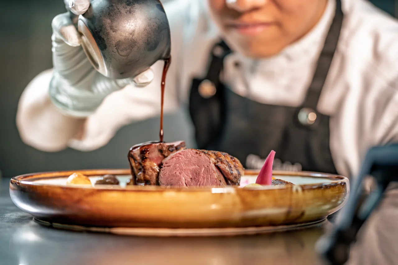 A chef pouring sauce over a plated dish