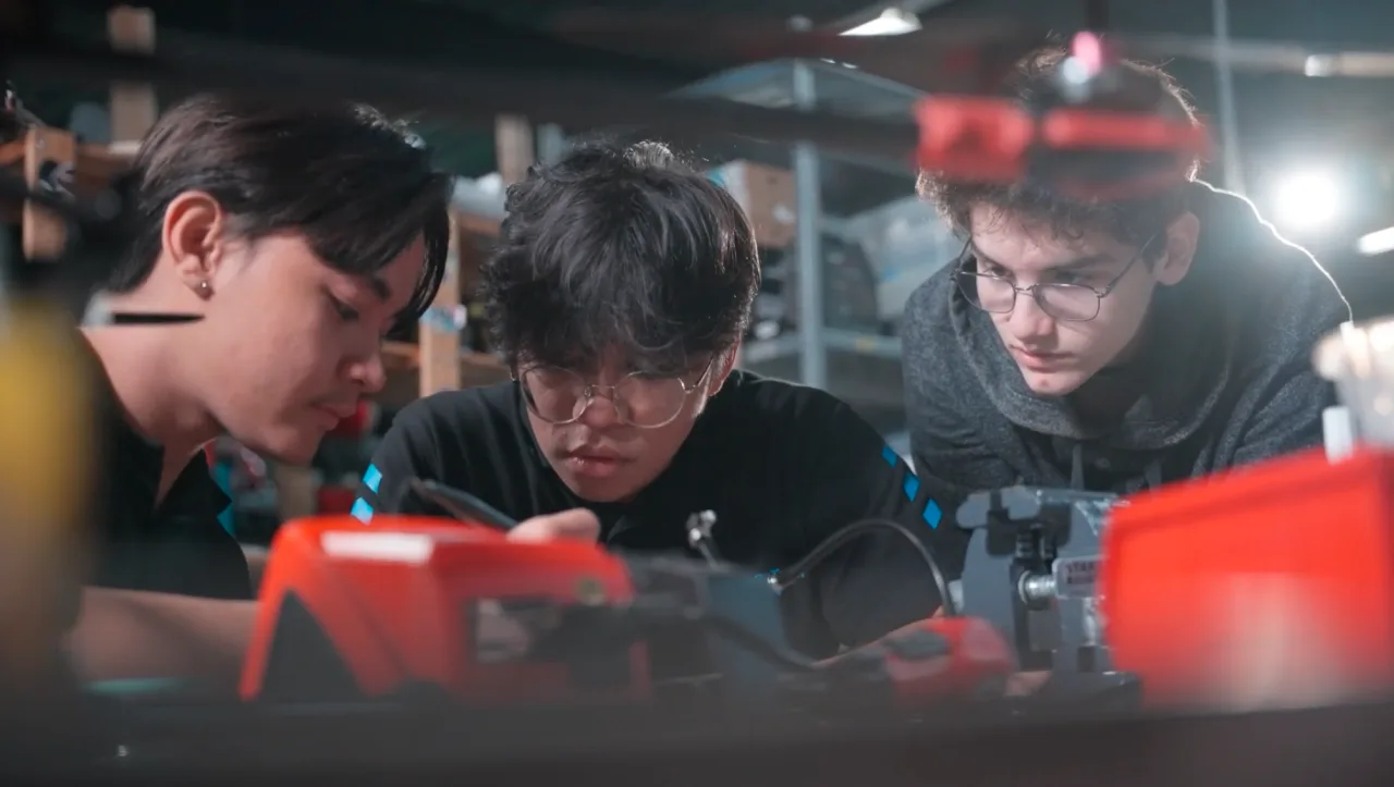 Three people working on equipment in a workshop