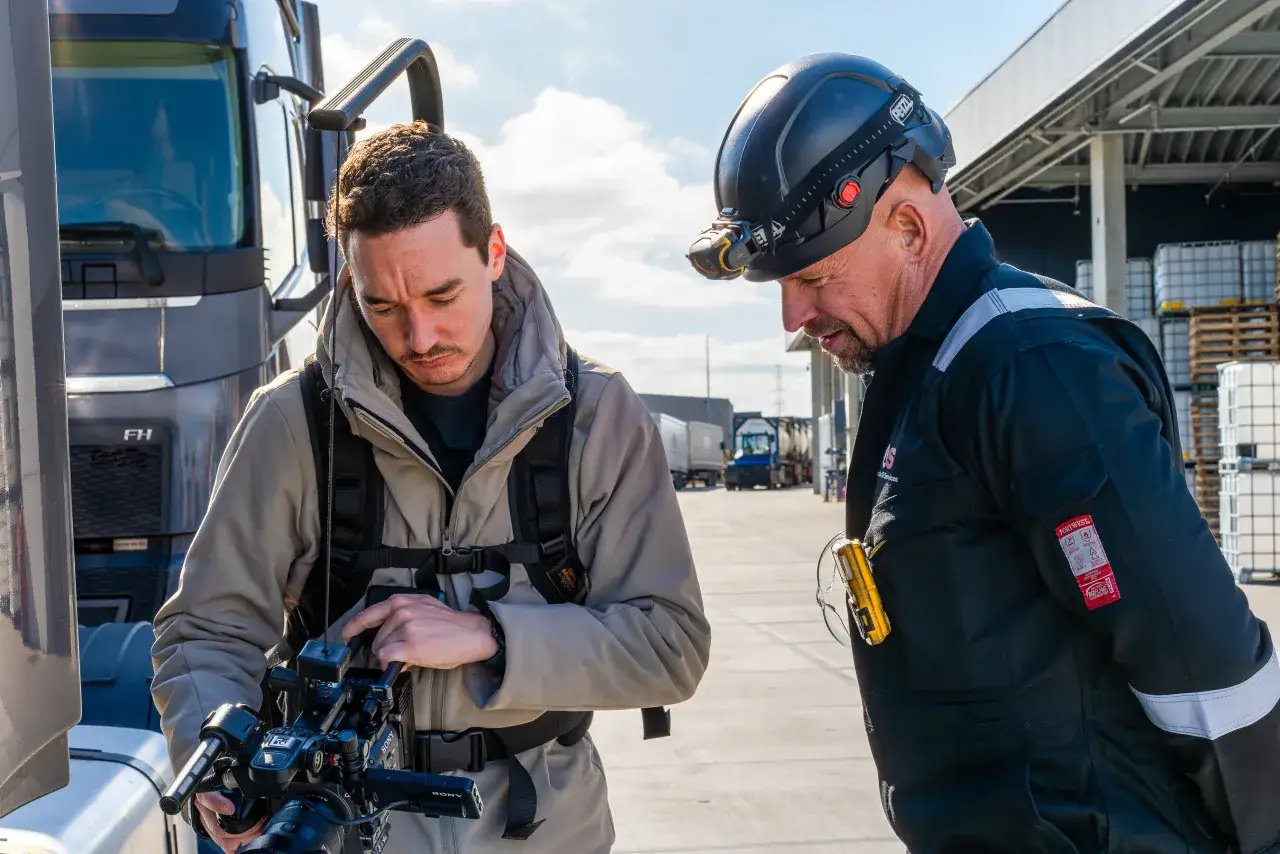 A camera operator filming alongside a driver at a logistics site