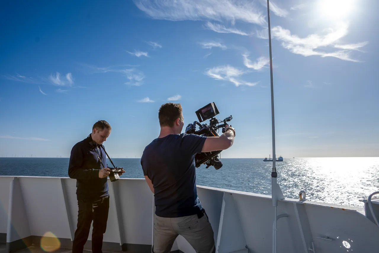 Two crew filming on the deck of a ship at sea